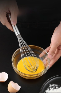 Close-up of stainless steel whisk mixing eggs in a glass bowl on black background