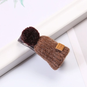 Close-up of a brown handmade plush hat hair clip on a white card with green leaves