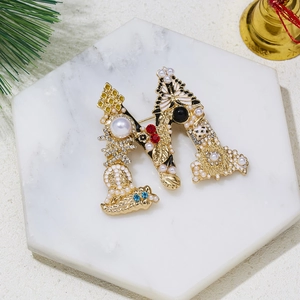 Golden letter M brooch with pearls and colorful rhinestones on marble tray decoration