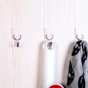 White plastic adhesive hooks with metal hangers mounted on wood wall for home organization