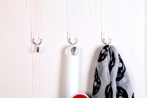 Three white adhesive wall hooks mounted on light wood surface hanging a scarf and tool