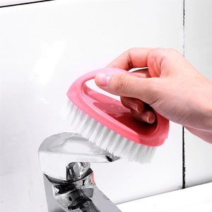 Pink egg-shaped laundry brush with handle cleaning a faucet on a white tile wall