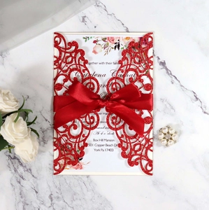 Macro shot of laser-cut red glitter wedding invitation with floral insert and silk ribbon