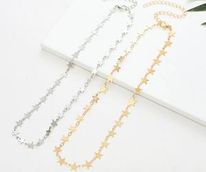 Detail of star charm necklace in gold and silver finish on a white tiered background