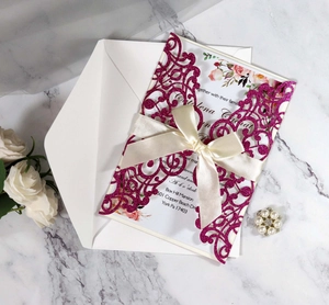 Detailed view of rose red laser cut wedding invitation with white ribbon and marble background