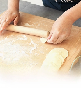 Close-up of a natural beech wood rolling pin being used on a flour-covered board