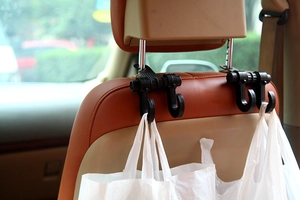 Detail of black double car seat hook holding a plastic bag on a leather headrest