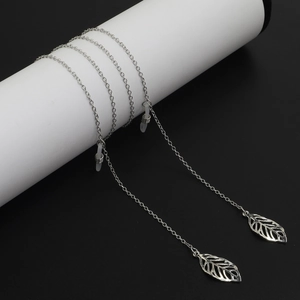 Silver metal eyewear chain with hollow leaf charms on a minimalist white cylinder stand