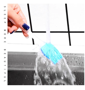 Close-up of cleaning a blue silicone oil brush with clear handle under running water