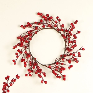 Couronne de Noël artificielle avec baies rouges et branches brunes sur un mur clair