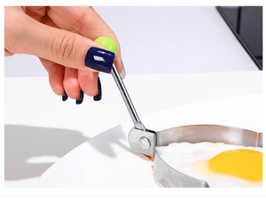 Close-up of heart-shaped stainless steel egg mold with a green handle in a frying pan