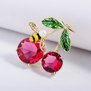 Detailed close-up of cherry brooch with red gems, green enamel leaves and pearl bee