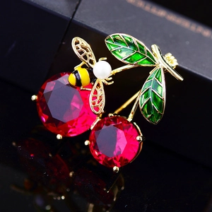 Close-up of enamel cherry brooch with red crystals, green leaf and pearl honeybee detail