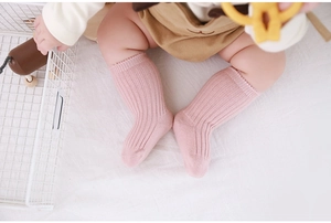 Close-up of pink knitted thick cotton baby socks on infant feet with white bedding background