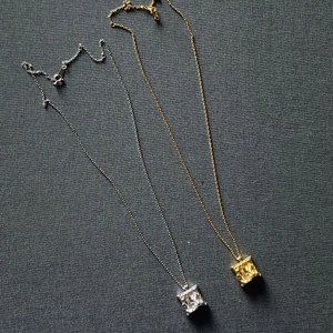 Close-up of square irregular texture pendants in gold and silver on grey fabric