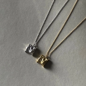 Macro shot of square necklaces with gold and silver rock textures on gray background