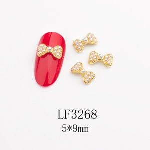 Détails de bijoux à ongles nœuds dorés 5x9mm avec perles sur manucure rouge et fond blanc