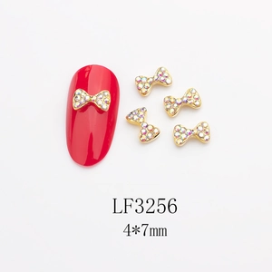 Détail de nœud doré pour nail art avec strass AB sur un ongle de présentation rouge