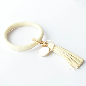 Close-up of cream leather keychain bracelet with tassel and round metal engraving tag
