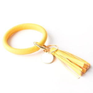 Detail of yellow leather bracelet keychain with gold tassel and white enamel tag