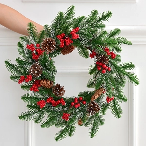 Weihnachtskranz mit grünen Tannennadeln, roten Beeren und Zapfen vor weißer Wand