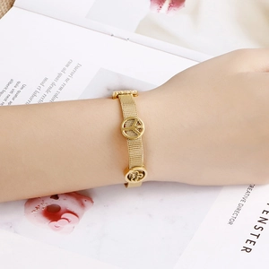 Adjustable gold mesh bracelet featuring peace sign and floral totem charms worn by model