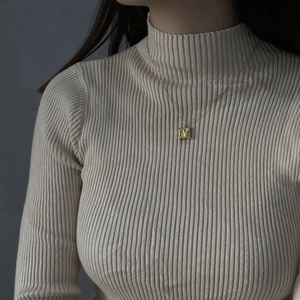 Detail shot of a golden square pendant with a unique textured surface on a fine chain