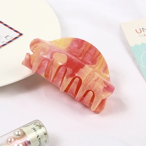 Macro detail of a marble-textured pink and yellow acrylic hair claw clip with subtle glitter
