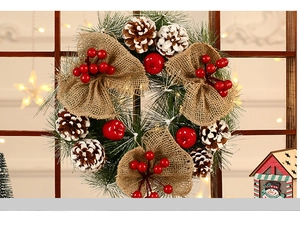Detail of Christmas wreath with pine needles, red berries, cones, and burlap bow decor