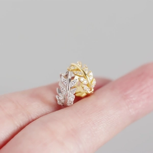 Close-up of olive leaf earrings with sparkling stones shown on a fingertip for size