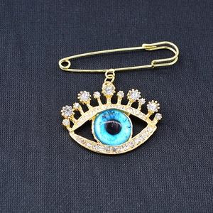 Golden evil eye brooch pin with blue crystal and rhinestones on grey fabric
