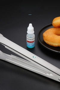 Détail d'une pince alimentaire en acier inoxydable 304 saisissant un donut sur fond noir
