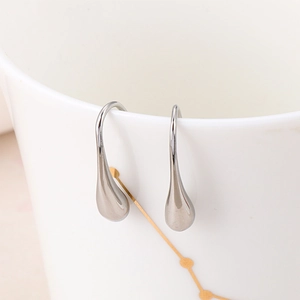 Polished silver stainless steel water drop earrings on a white ceramic cup
