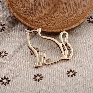 Detail of a minimalist gold cat brooch with hollow design on floral fabric background