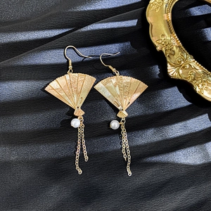 Detailed close-up of golden fan-shaped earrings with pearl accents and long tassels