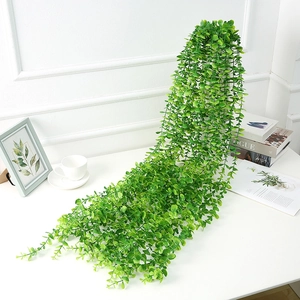 Detail of green faux eucalyptus trailing vine on a white wall with home decor accents