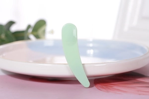 Macro view of a light green curved cosmetic spatula on a ceramic plate background