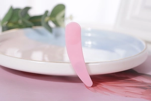 Close-up of pink crescent cosmetics applicator spoon resting on elegant ceramic plate