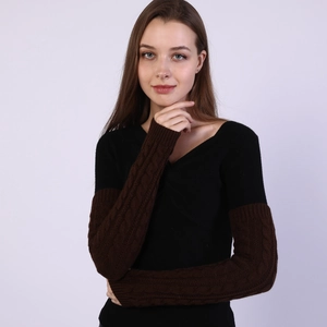 Detail of knitted arm warmers featuring brown cable stitch texture and black sleeve contrast