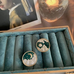 Detail of vintage round enamel earrings with sun and moon motifs on green velvet