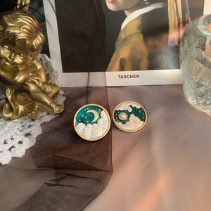 Macro detail of vintage moon and cloud earrings with green enamel and pearl accents
