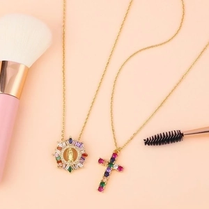 Gold Virgin Mary and cross necklaces with colorful cubic zirconia on a pink background