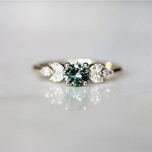 Macro detail of round emerald-green gemstone ring with marquise diamond side stones