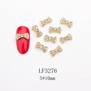 Dettaglio di ciondoli per unghie a fiocco oro 5x10mm con strass e manicure rossa