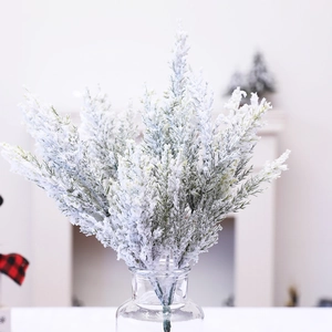 Artificial cedar branches with frosted snow in a glass vase on a cozy mantel background