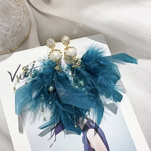 Detailed shot of teal feather earrings with faux pearls and sparkling crystal accents