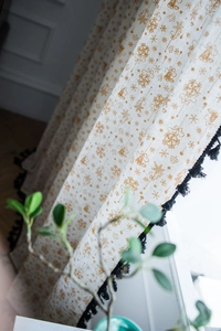 Detail of Christmas themed white cotton linen curtain with gold snowflake prints and black tassels