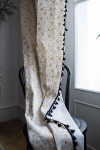 Detail of white cotton linen curtain with gold snowflake prints and black tassels on a chair