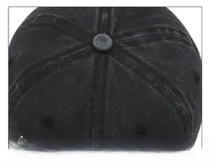 Detail of the stitched top button and seam structure on a washed black denim baseball cap