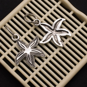 Vintage silver alloy starfish pendants with textured and smooth finishes on mesh stand